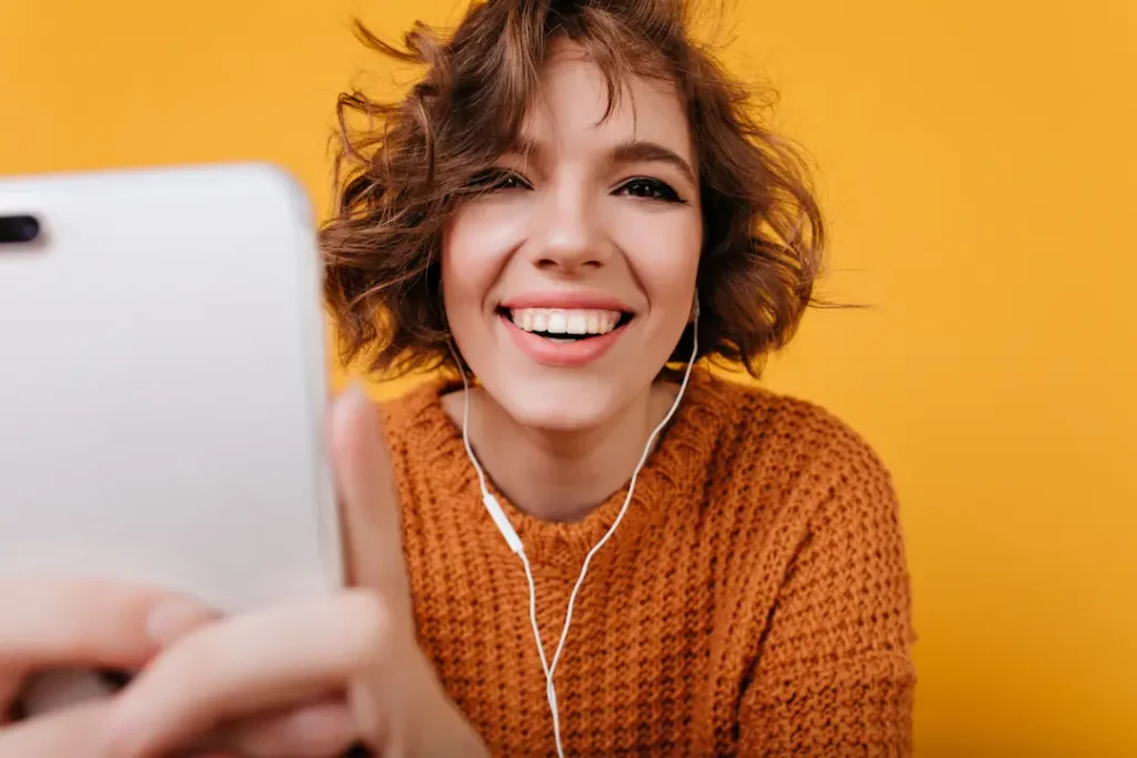 Primer plano de una joven creadora de contenido sonriente y auténtica con pelo rizado, haciéndose un selfie con fondo amarillo brillante, representando el carisma real en Matchis